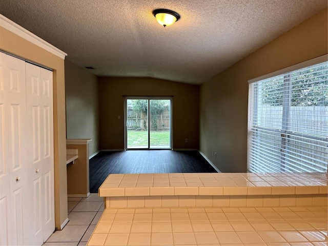 spare room with baseboards, visible vents, vaulted ceiling, a textured ceiling, and light tile patterned flooring