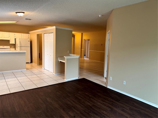 interior space with light tile patterned floors, visible vents, white cabinets, light countertops, and freestanding refrigerator