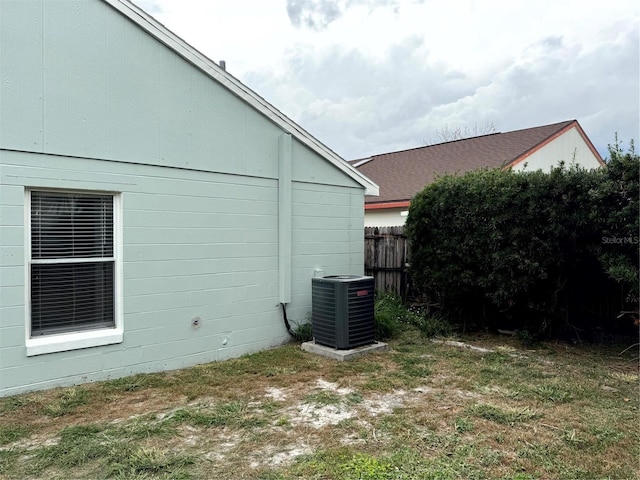 view of property exterior featuring a shingled roof, cooling unit, fence, and a lawn