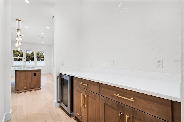 kitchen with recessed lighting, beverage cooler, a sink, hanging light fixtures, and light wood finished floors