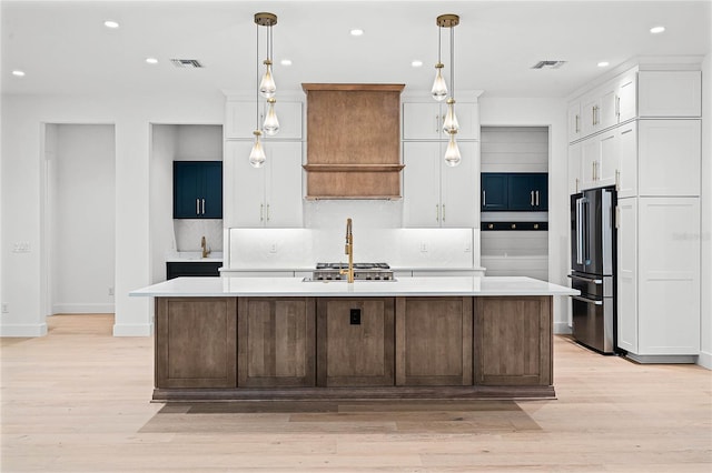 kitchen with a kitchen island with sink, high end refrigerator, white cabinetry, and light countertops