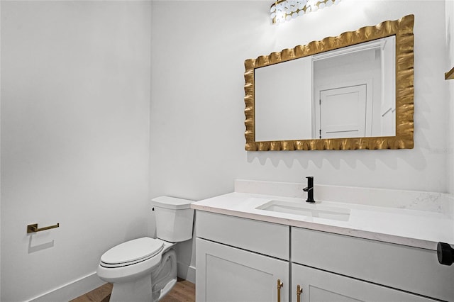 bathroom with toilet, wood finished floors, vanity, and baseboards