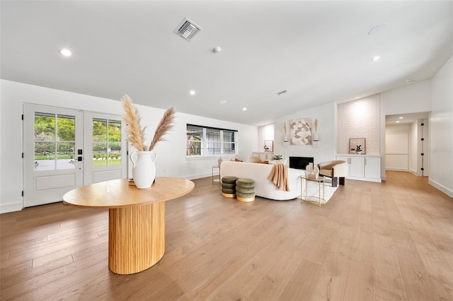 living area featuring light wood-style floors, a fireplace, visible vents, and vaulted ceiling