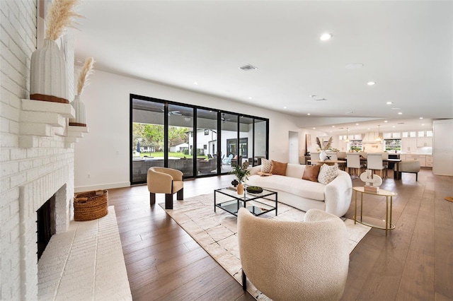 living area featuring light wood-style flooring, recessed lighting, visible vents, baseboards, and a brick fireplace