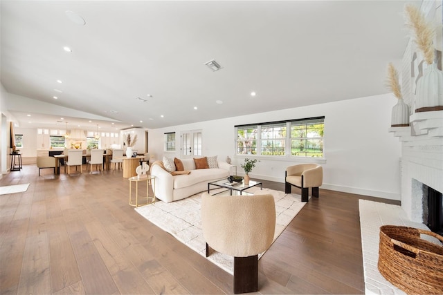 living area with a brick fireplace, visible vents, vaulted ceiling, and light wood finished floors