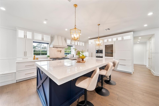 kitchen with a large island, visible vents, custom range hood, glass insert cabinets, and white cabinets