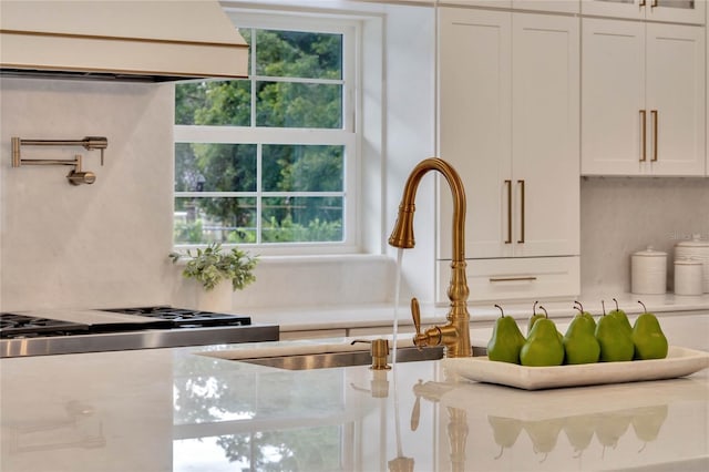 interior details with a sink, custom exhaust hood, white cabinets, and light countertops