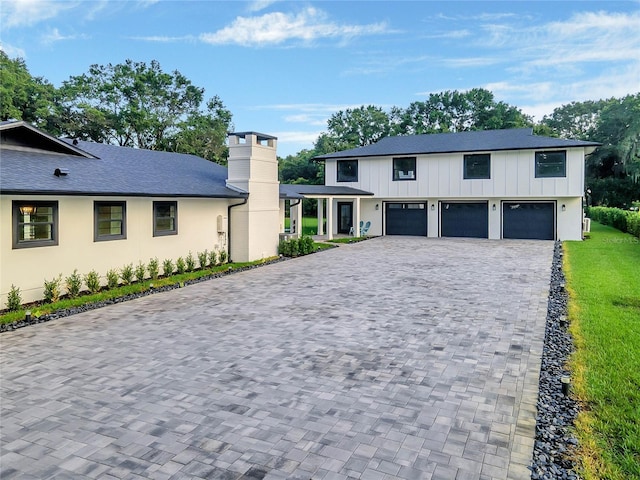 view of front of property with board and batten siding, decorative driveway, a chimney, and an attached garage