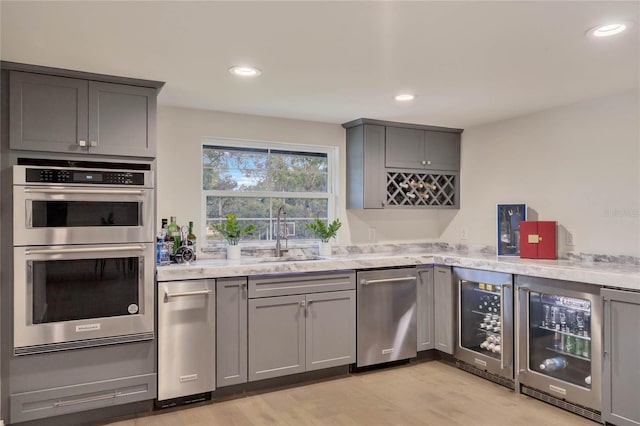 kitchen with beverage cooler, gray cabinets, stainless steel double oven, and a sink