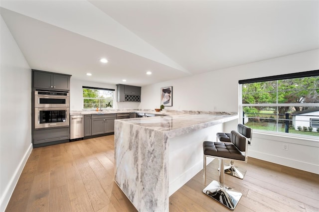 kitchen with a breakfast bar, lofted ceiling, gray cabinetry, double oven, and a peninsula