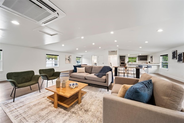 living room with baseboards, lofted ceiling, a wall mounted air conditioner, light wood-type flooring, and recessed lighting