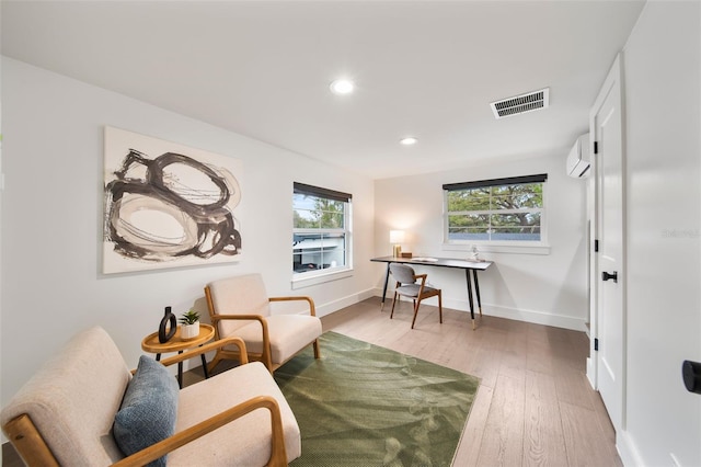 sitting room with light wood-type flooring, baseboards, visible vents, and a wall mounted AC