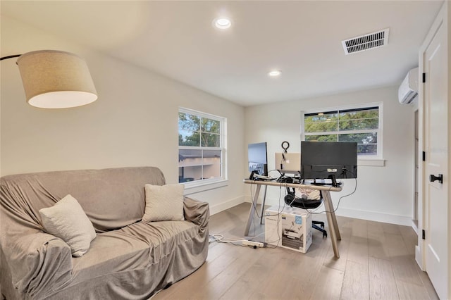 home office with light wood-style flooring, a wall mounted air conditioner, visible vents, and baseboards