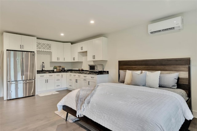 bedroom featuring recessed lighting, freestanding refrigerator, an AC wall unit, a sink, and wood finished floors