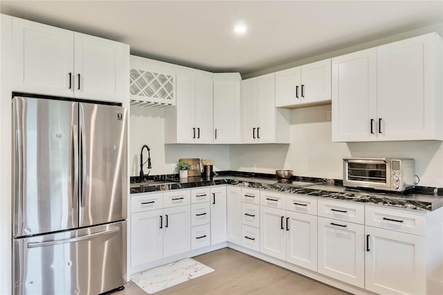 kitchen featuring dark stone counters, freestanding refrigerator, white cabinets, and a sink