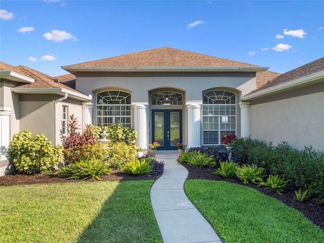 property entrance featuring french doors, roof with shingles, a yard, and stucco siding