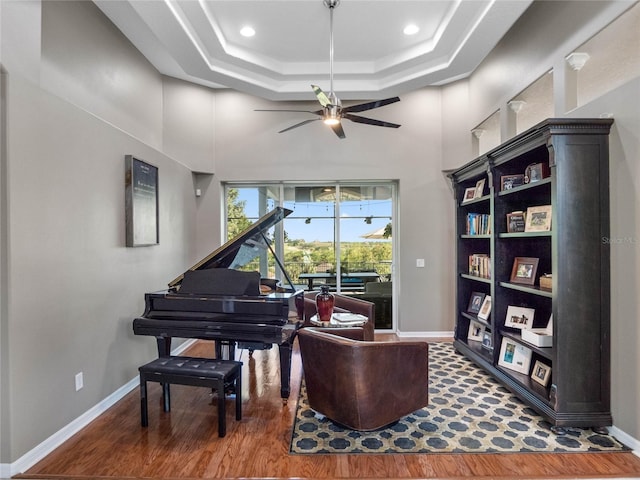 living area featuring a ceiling fan, baseboards, a raised ceiling, and wood finished floors