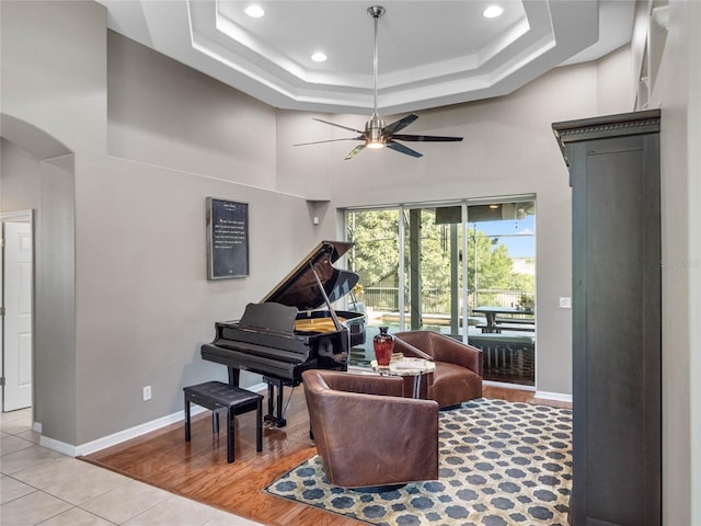 living area with arched walkways, a raised ceiling, a towering ceiling, a ceiling fan, and baseboards