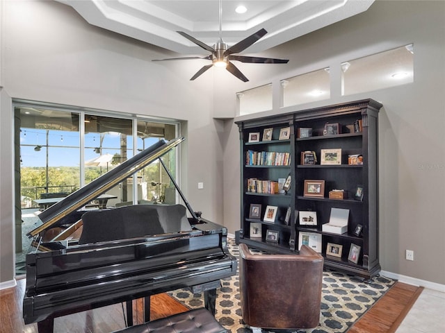 sitting room featuring a high ceiling, baseboards, a raised ceiling, and a ceiling fan