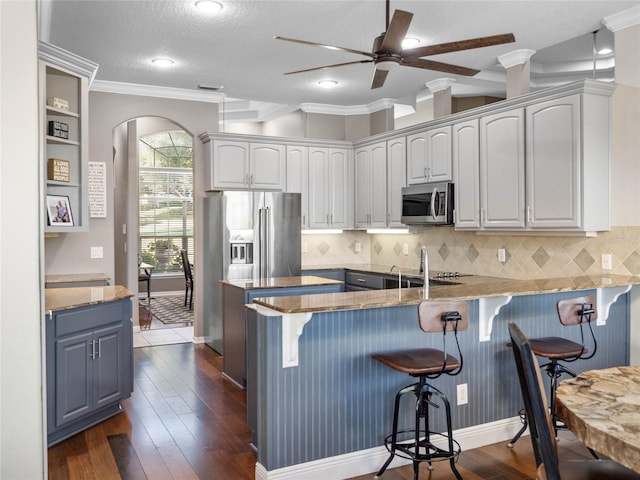 kitchen featuring arched walkways, stainless steel appliances, a peninsula, dark wood-style flooring, and white cabinets