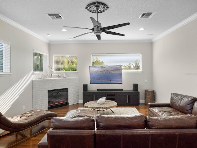 living area with a glass covered fireplace, wood finished floors, visible vents, and crown molding