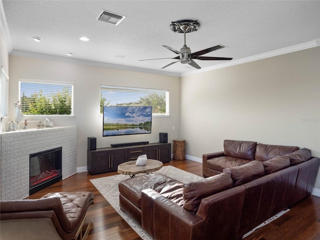 living room featuring baseboards, visible vents, a glass covered fireplace, ornamental molding, and dark wood-style flooring