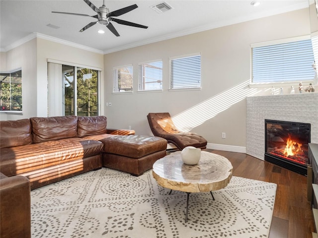 living area featuring visible vents, ornamental molding, a glass covered fireplace, wood finished floors, and baseboards