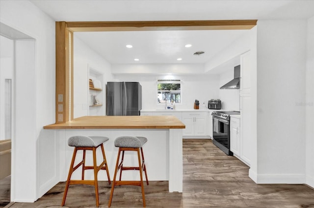 kitchen with stainless steel appliances, white cabinets, light countertops, wall chimney exhaust hood, and a kitchen bar