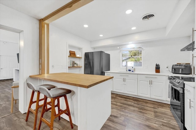 kitchen with butcher block counters, stainless steel electric range, freestanding refrigerator, and white cabinetry