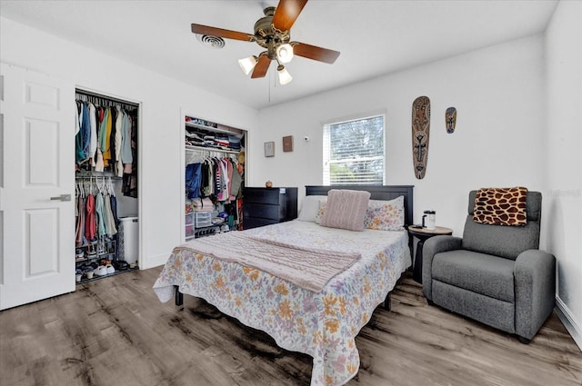 bedroom with wood finished floors, ceiling fan, baseboards, and two closets