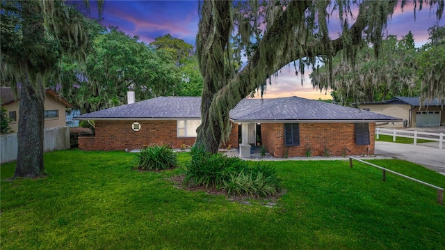 ranch-style home featuring brick siding, fence, a chimney, and a front lawn