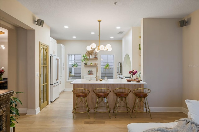 kitchen with a peninsula, high end white fridge, light countertops, open shelves, and a kitchen bar