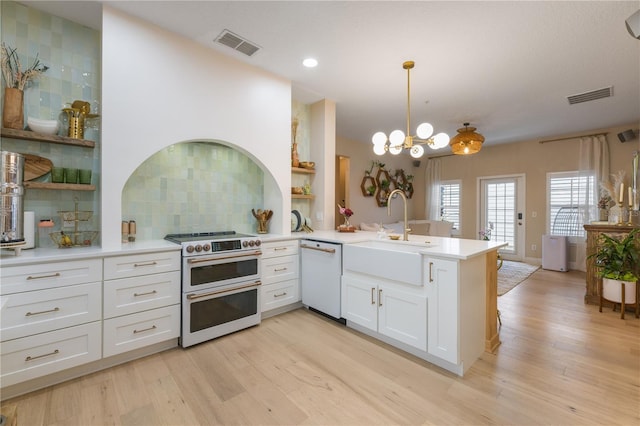 kitchen featuring a peninsula, light countertops, double oven range, dishwasher, and decorative light fixtures