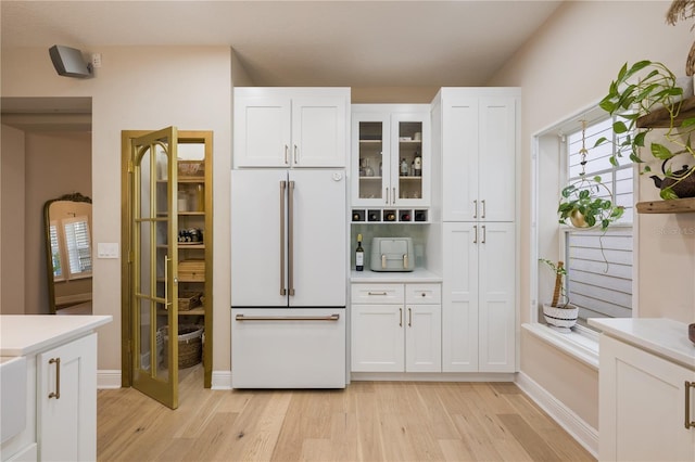 kitchen with white cabinets, light countertops, high end white refrigerator, light wood finished floors, and glass insert cabinets