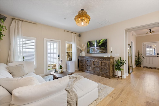 living area featuring light wood finished floors, crown molding, visible vents, and a notable chandelier