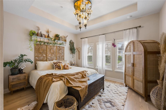 bedroom featuring light wood-type flooring, baseboards, a raised ceiling, and a notable chandelier