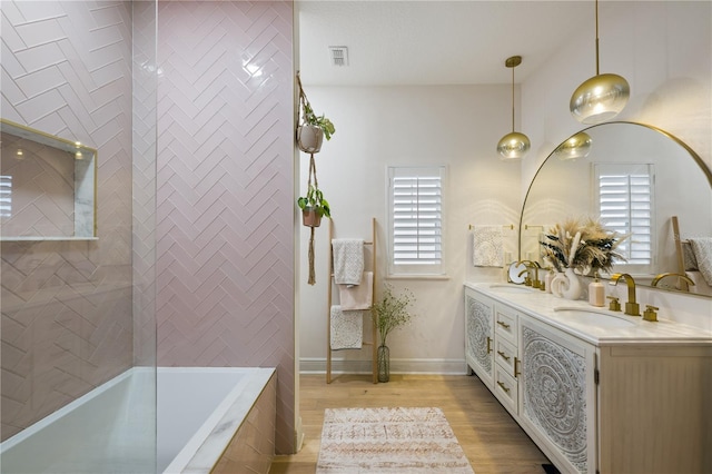 bathroom featuring a relaxing tiled tub, double vanity, a sink, and wood finished floors