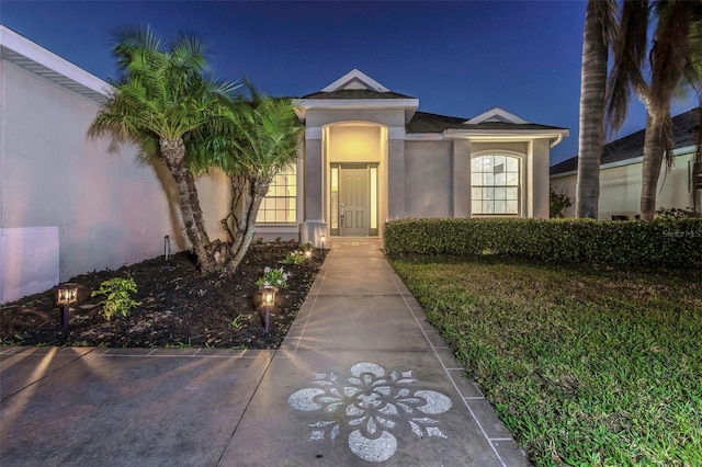 exterior entry at night with a yard and stucco siding