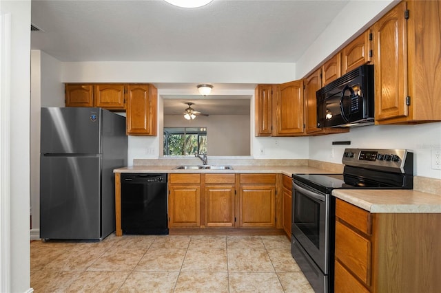 kitchen with light tile patterned floors, brown cabinets, light countertops, black appliances, and a sink