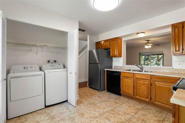 kitchen with black dishwasher, brown cabinets, freestanding refrigerator, washing machine and dryer, and a sink