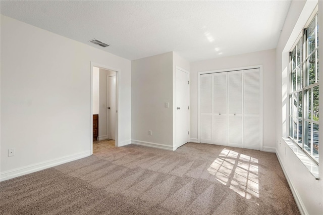 unfurnished bedroom featuring a textured ceiling, visible vents, baseboards, a closet, and carpet