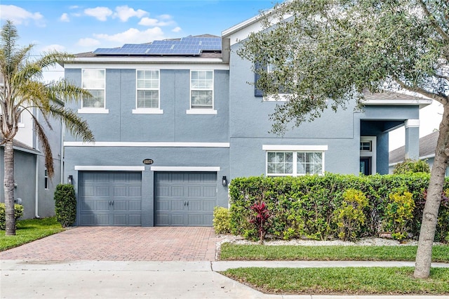 view of front facade with a garage, decorative driveway, stucco siding, and solar panels