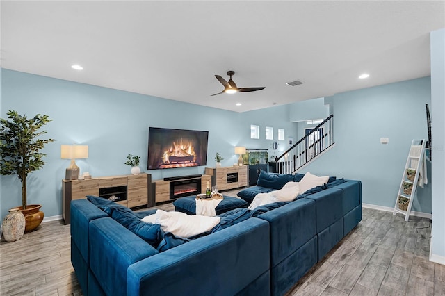 living room featuring stairs, light wood-style flooring, a glass covered fireplace, and visible vents