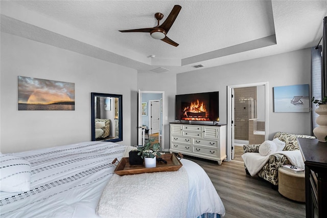 bedroom featuring a tray ceiling, dark wood finished floors, a textured ceiling, and ensuite bathroom