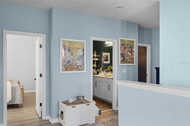 hallway with a sink, light wood finished floors, baseboards, and a textured ceiling