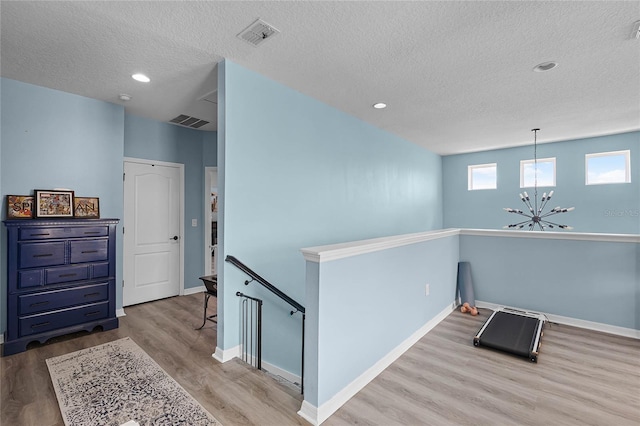 hallway featuring visible vents, a chandelier, wood finished floors, and an upstairs landing