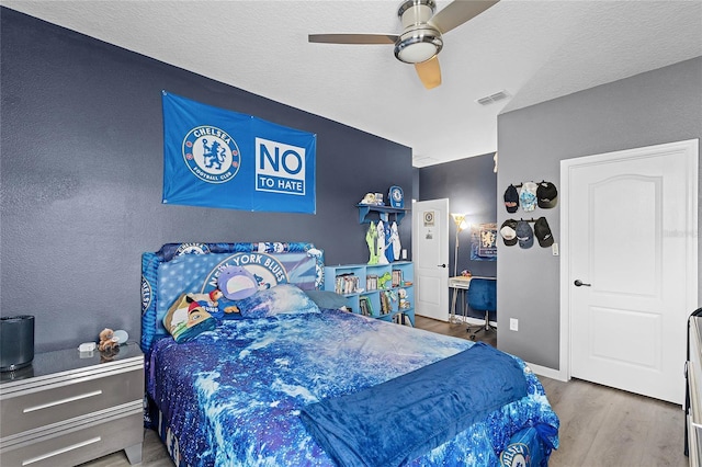 bedroom featuring baseboards, visible vents, a ceiling fan, wood finished floors, and a textured ceiling