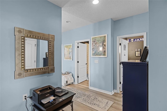 corridor featuring baseboards, light wood-style flooring, and a textured ceiling