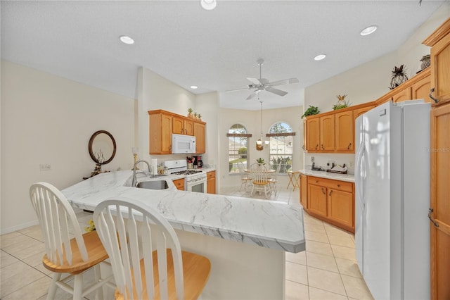 kitchen with a breakfast bar, light countertops, a sink, white appliances, and a peninsula