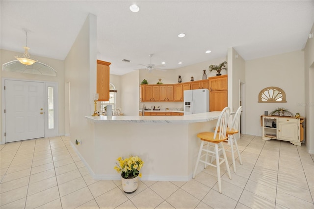 kitchen featuring a breakfast bar area, light tile patterned flooring, a peninsula, light countertops, and white fridge with ice dispenser